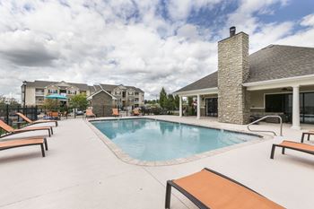 A pool surrounded by lounge chairs and a building in the background.